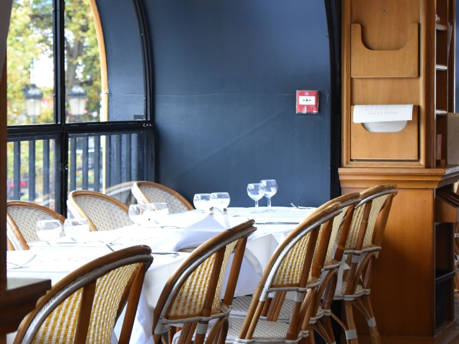 Sala del bistró con sillas de rejilla, mesas vestidas de blanco y la pared azul del fondo